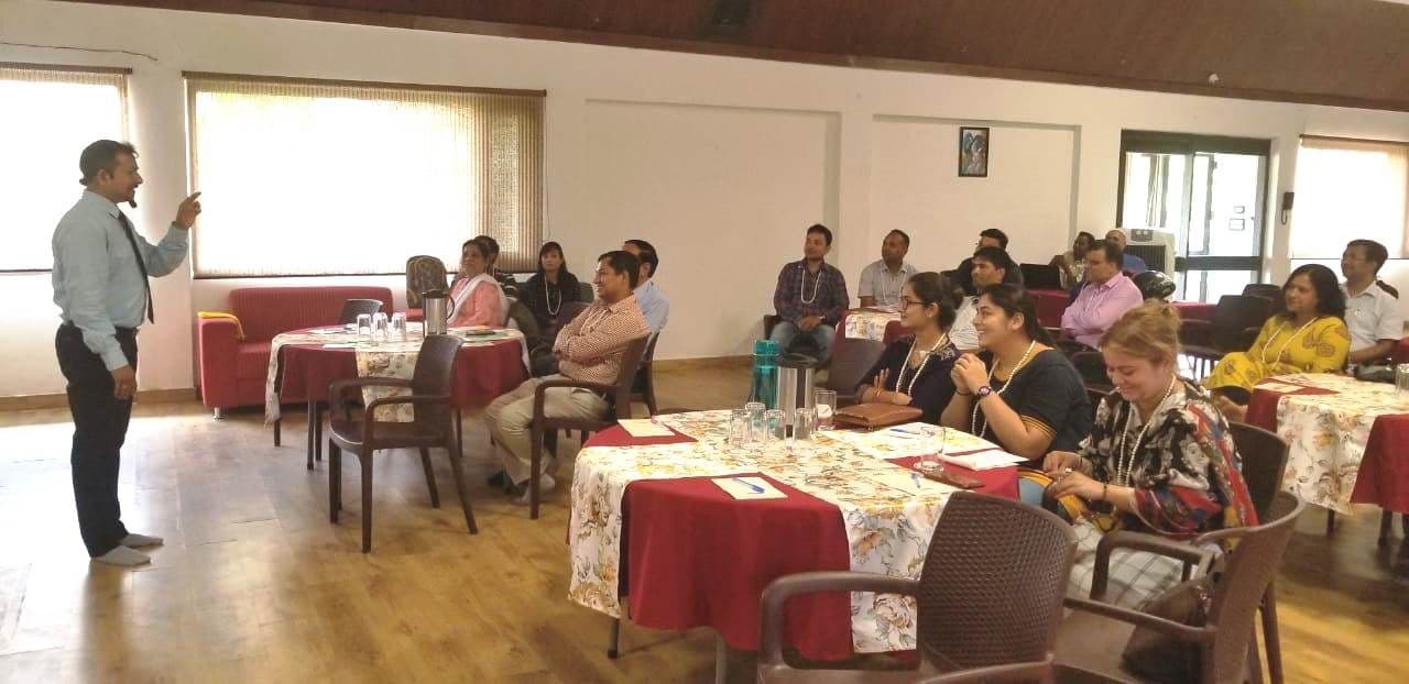 A training session in progress, with participants seated at tables facing the trainer.